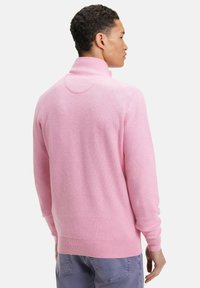 Pull rose clair avec un col montant, un motif en maille texturé, et des poignets et un ourlet côtelés. Le dos présente un détail d'accent circulaire.