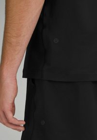 Tricou sportiv negru cu mâneci scurte, cusături plate și detalii cu logo pe lateral. Asortat cu șorturi negre. 