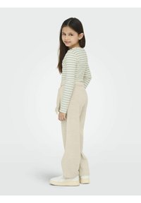 Randig långärmad topp i ljuskräm med gröna ränder, ihop med beiga linnebyxor och vita sneakers med kraftiga sulor.