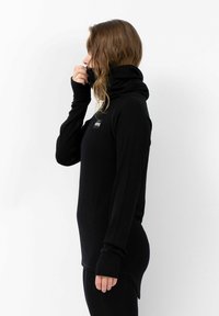 Schwarzes Langarmoberteil mit hohem Kragen, gerippter Textur und Daumenlöchern, versehen mit einem kleinen Logo auf der Brust. Schlankes Design.