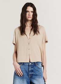 Chemise à manches courtes beige à boutons, coupe décontractée et texture douce, associée à un jean en denim bleu avec une finition délavée.