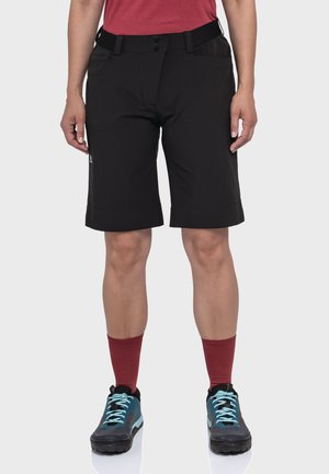 Schwarze Outdoor-Shorts mit geradem Schnitt, zwei vorderen Taschen und einemBund mit zwei Knöpfen. Kombiniert mit roten Socken und blauen Schuhen.
