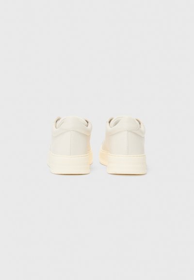 Beige nahkalimput, joissa on pyöreä kanta, kontrastina oleva kerma rubber-pohja, ja pehmustettu kaulus. Suora pinta, minimalistinen muotoilu.
