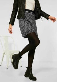 Černobíle vzorovaná sukně, doplněná černými punčochami a kotníkovými botami. Outfit zahrnuje přiléhavý černý kožený kabát.