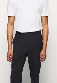 Czarne casualowe spodnie z elastycznym paskiem, gładką fakturą i kieszeniami po bokach, zestawione z gładkim białym t-shirtem z krótkim rękawem.