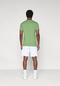 Πράσινο βαμβακερό t-shirt με κοντά μανίκια, λαιμόκοψη τύπου crew και χαλαρή εφαρμογή, συνδυασμένο με λευκά σορτς. Απλός σχεδιασμός μονόχρωμος, χωρίς ορατά σχέδια.