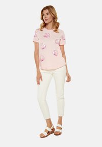 Lyserød kortærmet t-shirt med muslingemønstre. Sammen med hvide slim-fit bukser og brune platform sandaler med hvide stropper.