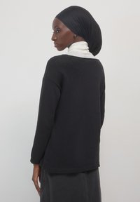 Maglione nero con texture, dalla vestibilità rilassata, maniche lunghe e orlo arrotondato, abbinato a un top bianco con colletto alto sotto.