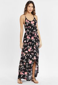 Rochie maxi florală cu un fundal negru, având flori roz și albe, bretele subțiri, talie cu șnur și o fanta laterală înaltă.
