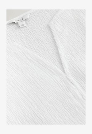 Biała teksturowana tkanina ubrania z dekoltem w serek i metką marki "NEXT" z oznaczeniem "Made in Turkey".