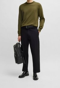 Oliwkowy sweterek dzianinowy, czarne spodnie, skórzane buty i fakturowany czarny plecak. Prosty, prosty design z gładkim wykończeniem.