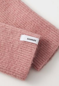 Roosa kudumine villakangas ribide tekstuuriga. Valge kangasilt musta tekstiga "SAMSØE", mis on külge kinnitatud.