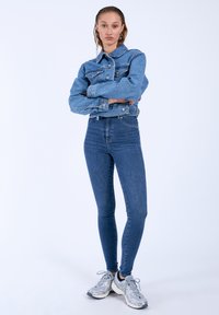 Jeansjacka och högmidjade blåjeans. Jackan har en klassisk krage och knappstängningar, medan jeansen har en slim fit. Silverfärgade sneakers.