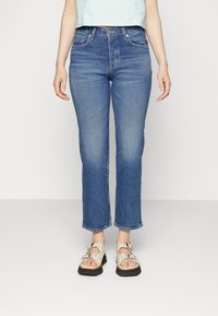 Blue straight-leg jeans with a slightly faded wash, front pockets, and belt loops, paired with light-colored patterned sandals.