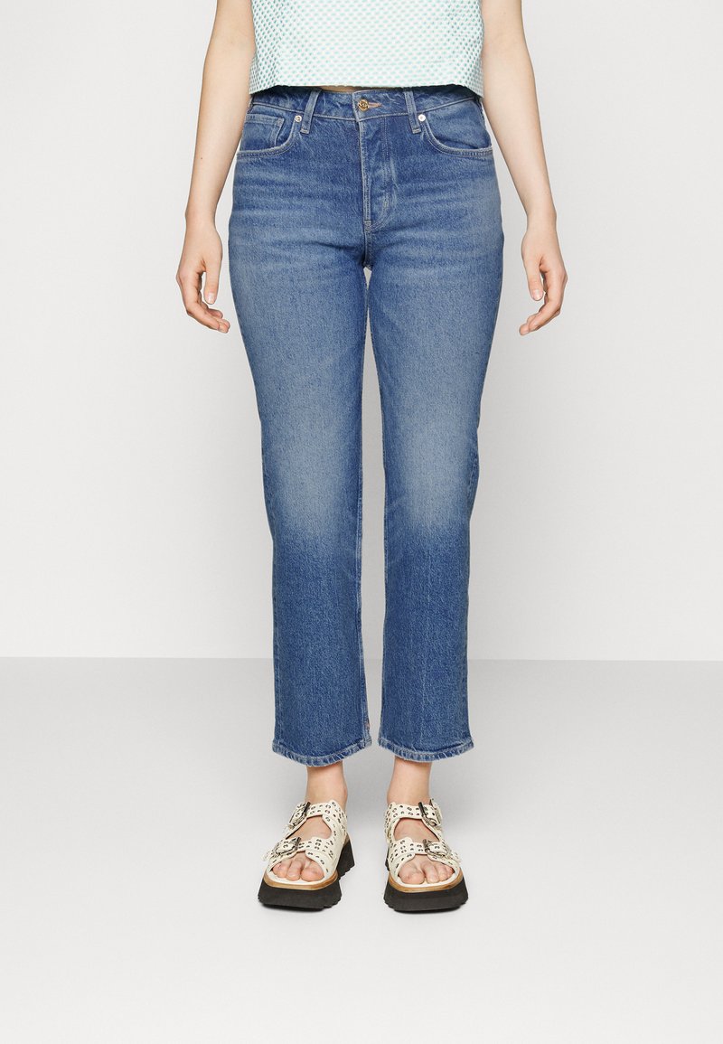 Blue straight-leg jeans with a slightly faded wash, front pockets, and belt loops, paired with light-colored patterned sandals.
