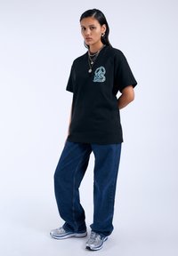 Camiseta de algodón negra con un gráfico en azul claro en el pecho, combinada con unos vaqueros de mezclilla azules holgados y zapatillas deportivas plateadas.