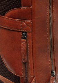 Zaino in pelle marrone con pannelli in rete testurizzata, cuciture a contrasto e doppi zip con targhette marchiate per un tocco di dettaglio in più.