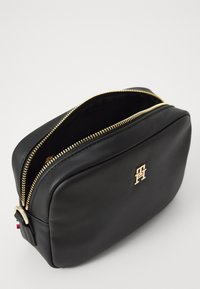 Trousse de maquillage en cuir noir avec une fermeture éclair dorée, de forme rectangulaire, et logo embossé sur le devant. Présente des accents de quincaillerie dorés.