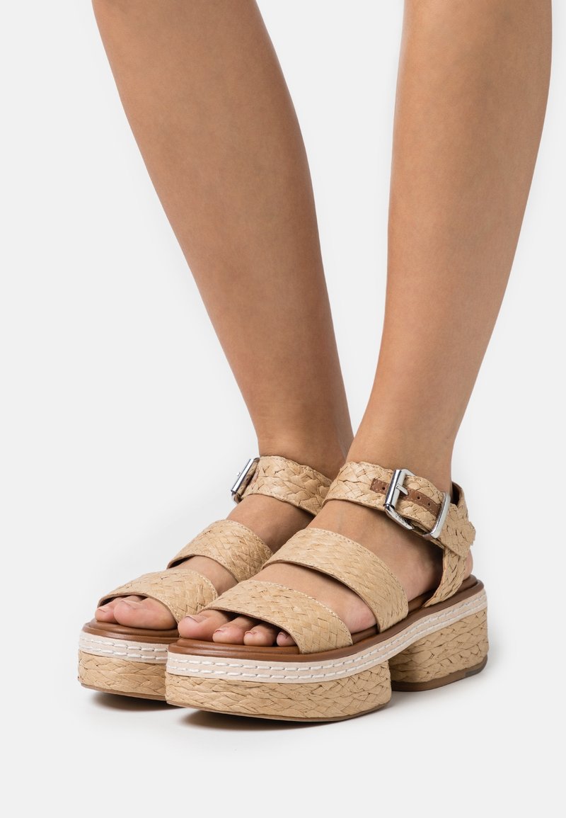 Plattform sandaler med vävda beige remmar, en tjock sula med texturerad yta och metallspännen för justering.