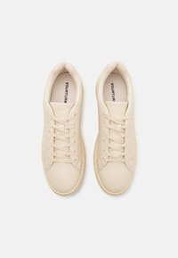 Sneakers beige chiaro realizzati in morbida pelle sintetica, caratterizzati da un classico design con lacci, punta tonda e dettagli di cucitura discreti.