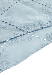 Tissu bleu clair avec motifs floraux brodés et petites découpes circulaires le long des bords.