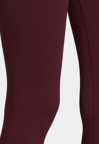 Bordowe legginsy wykonane z elastycznego materiału, charakteryzujące się gładką teksturą i dopasowanym krojem, bez widocznych wzorów czy elementów metalowych.