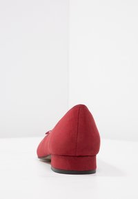 Chaussure basse en daim rouge à talon bas avec un bout pointu et un design minimaliste, dotée d'un petit talon noir et sans pièce métallique ni accent visible.
