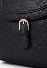 Schwarze Handtasche aus Leder mit strukturierter Oberfläche, ausgestattet mit einem goldfarbenen Schnallenakzent und einem abgerundeten Klappverschluss.