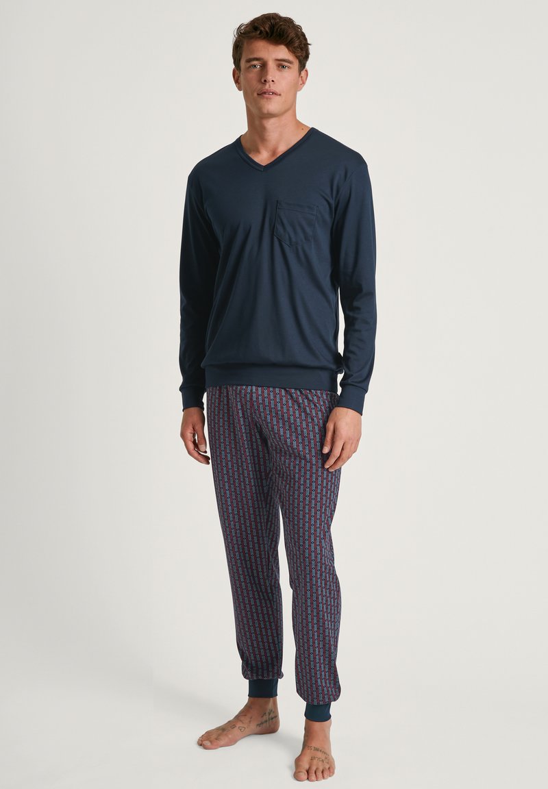 Marineblauwe lange mouwen V-hals top met zak; gemusterde pyjamabroek in blauw en bordeauxrood met opgerolde enkels. Gladde katoenmix stof.