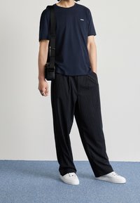 Námořnické bavlněné tričko s malým logem, kombinované s černými pruhovanými kalhotami a bílými teniskami. Doplňky zahrnují černou crossbody tašku.