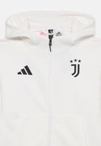 Hanorac alb cu fermoar, realizat dintr-un material moale. Prezintă logo-ul negru Adidas și emblema Juventus, cu glugă ajustabilă și buzunare frontale.