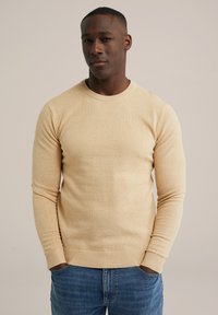 Pulover tricotat de culoare galben deschis cu guler rotund și mansete cu model, asortat cu blugi din denim albastru. Textura pare moale și ușor texturată.