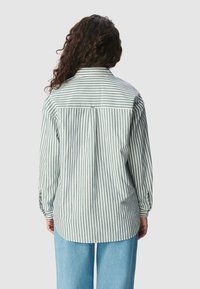 Gestreept shirt met een plooien aan de achterkant, gekenmerkt door verticale groene en witte strepen, lange mouwen en een kraag. Gecombineerd met losse, lichtblauwe broeken.