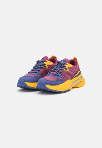 Colorful sneakers featuring a mix of purple, yellow, and blue materials, with textured surfaces, prominent laces, and a chunky outsole design.