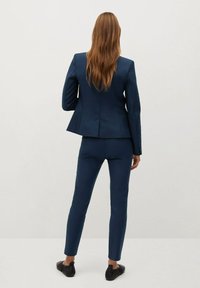 Navy blue tailored suit made of smooth fabric. Features a fitted blazer with a structured back and slim-fit trousers. Plain design, no patterns.