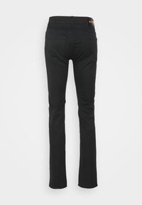 Jean noir slim avec poches arrière et petite pièce en cuir marron estampillée "BOSS" sur la ceinture, vu de dos.
