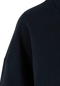 Felpa di un navy scuro con una texture morbida, caratterizzata da una vestibilità rilassata e un design a spalla cadente. Tessuto liscio con dettagli di cucitura minimi.