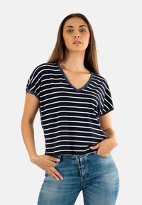 Camiseta de manga corta a rayas en azul marino y blanca con escote en V, con ribete azul en el cuello y las mangas. Combinada con pantalones vaqueros azules claros con botones.