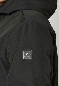 Giacca nera con una texture liscia, caratterizzata da un patch con il logo Kaporal sulla manica, che mette in risalto il suo design minimalista.