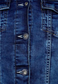 Buttoned denim jacket section, featuring dark blue fabric, visible stitching, silver hardware, and two chest pockets.
