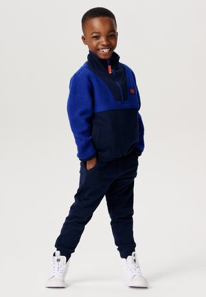 Navyblauwe en koningsblauwe fleece pullover met een halve rits, gecombineerd met bijpassende joggers. Witte sneakers maken de outfit compleet.