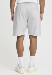 Shorts gris en mélange de coton avec une ceinture élastique, présentant une seule poche arrière et une longueur mi-cuisse. Portés avec des baskets blanches et des chaussettes.
