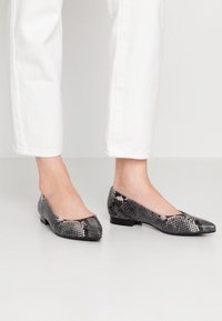 Płaskie buty o czarno-białym wzorze wężowym, z zaokrąglonym czubkiem i niskim obcasem. Wykonane z materiału przypominającego skórę.