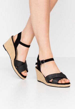 Sorte kilehæls-sandaler med en flettet jutesål, der har krydsstropper og ankelstropper i sort tekstureret materiale med en metalspænde.