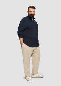 Marineblauwe gewatteerde pullover met een ritskraag, gecombineerd met beige corduroy broek en crèmekleurige sneakers. Eenvoudig en casual ontwerp.