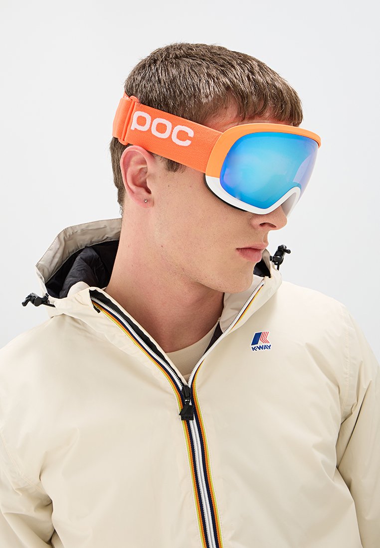 Pomarańczowe gogle narciarskie z szerokim niebieskim szkiełkiem, wyłożone pianką i z regulowanym paskiem. Noszone z beżową kurtką na zamek, z kolorowymi paskami.
