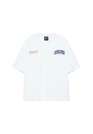 T-shirt blanc à manches courtes avec texte bleu marine "GOOD VIBES LAUNDROMAT" et texte rouge sur la poitrine, fond uni.