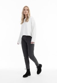 Felpa bianca corta con maniche ampie, abbinata a jeans aderenti grigi scuri e stivali neri con lacci alla caviglia. Design semplice e pulito.