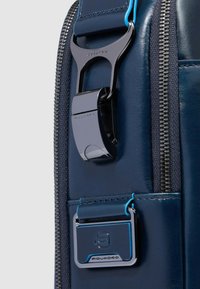 Borsa in pelle blu navy con fibbia e targhetta in metallo argentato e blu. Dotata di una cerniera robusta e dettagli testurizzati sul corpo.