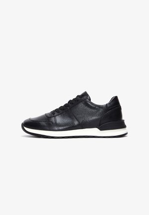 Baskets en cuir noir avec surface texturée, devant à lacets, semelle intermédiaire blanche et semelle extérieure en caoutchouc noir, présentées en profil latéral sur fond blanc.